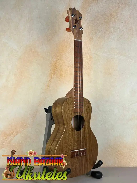 Wooden KoAloha Opio Concert Ukulele on a black stand showcasing solid acacia design