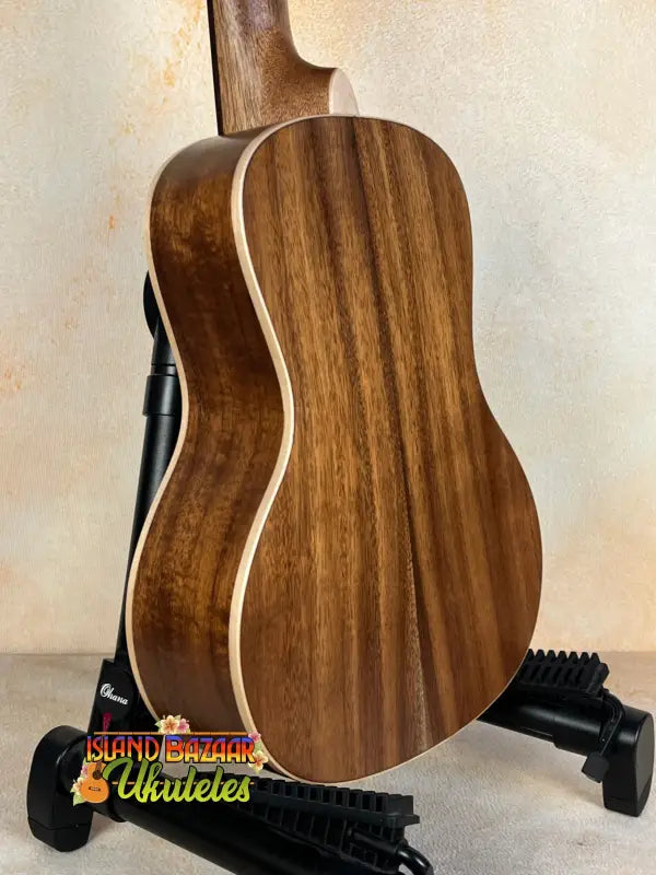 Acoustic guitar with walnut wood back on stand, highlighting Kala SA-C Concert Ukulele design