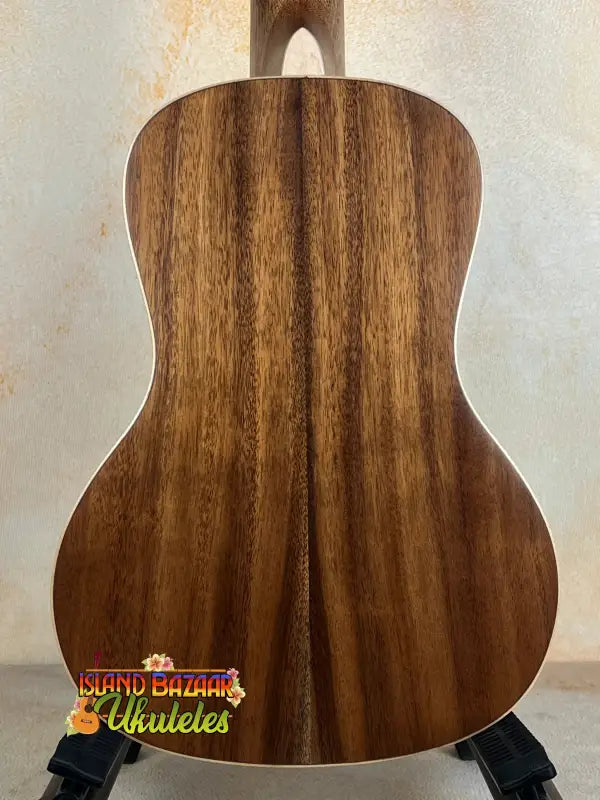 Acoustic guitar with wooden back panel on a stand, featuring Kala SA-C Concert Ukulele design