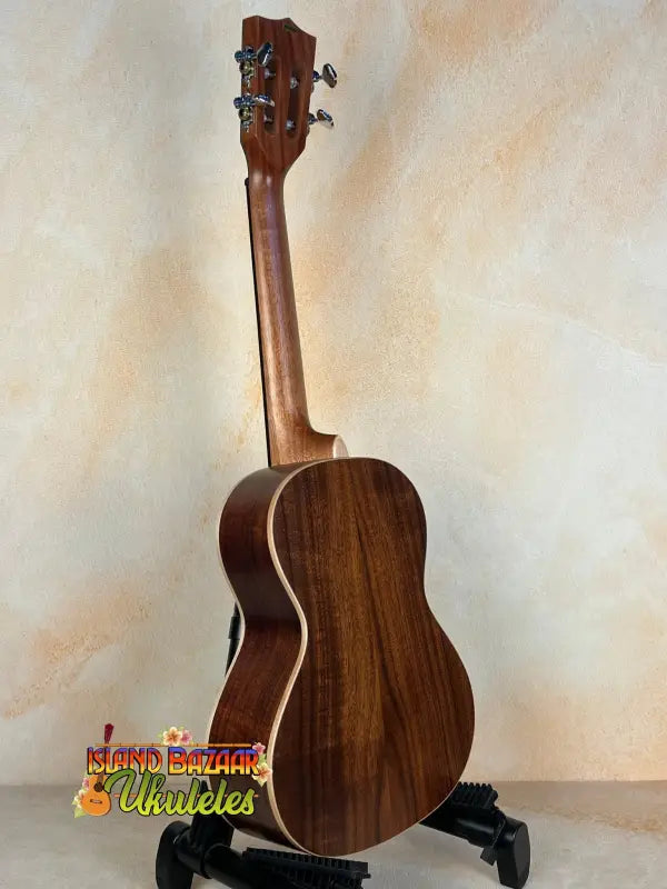 Wooden acoustic guitar on a stand near Kala SA-T Tenor Ukulele, showcasing rich design