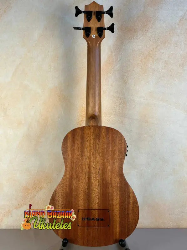 Wooden Kala U-Bass Nomad Acoustic-Electric Bass Ukulele on stand with black tuning pegs