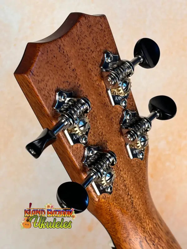 Guitar headstock with black tuning pegs on wood, featuring Kanile’a K3-T Tenor Koa Ukulele