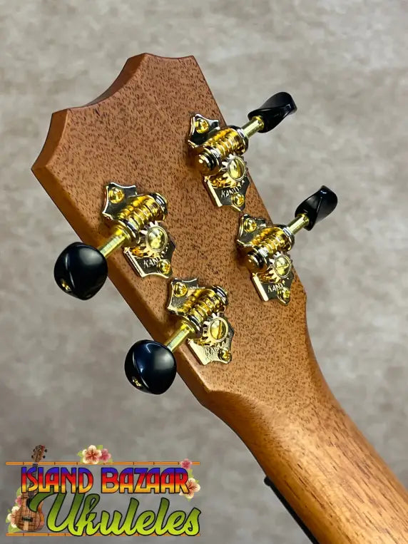 The headstock of a light brown solid mango kanilea kpa pro tenor ukulele with gold tuning machines and black pegs