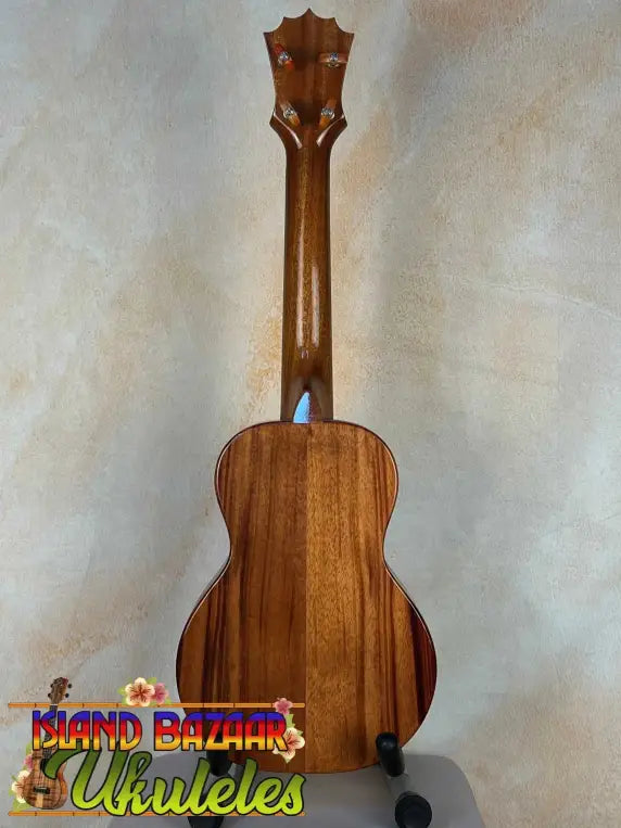 Wooden ukulele with decorative headstock on stand, showcasing KoAloha KCM-00 Concert design