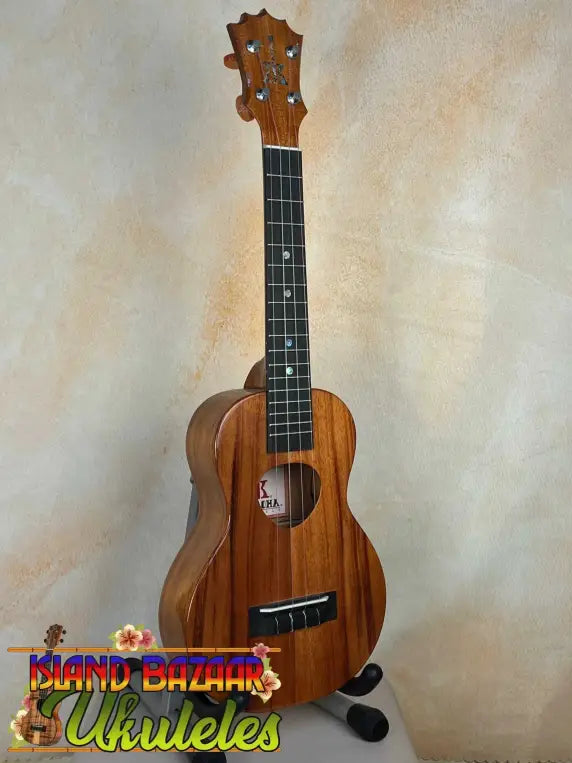 Wooden ukulele with natural finish on stand; KoAloha KCM-00 Concert, Solid Hawaiian Koa