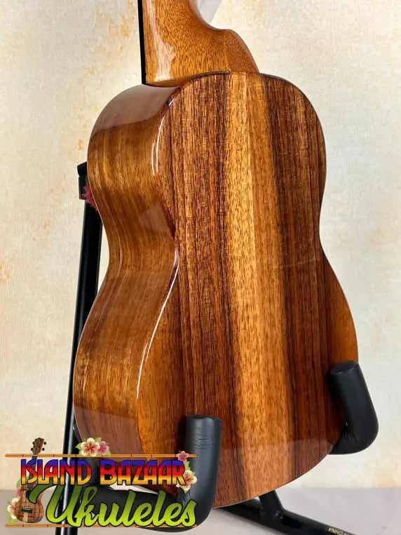 Wooden ukulele with rich brown grain on stand, featuring Hawaiian Koa and Ebony Fretboard