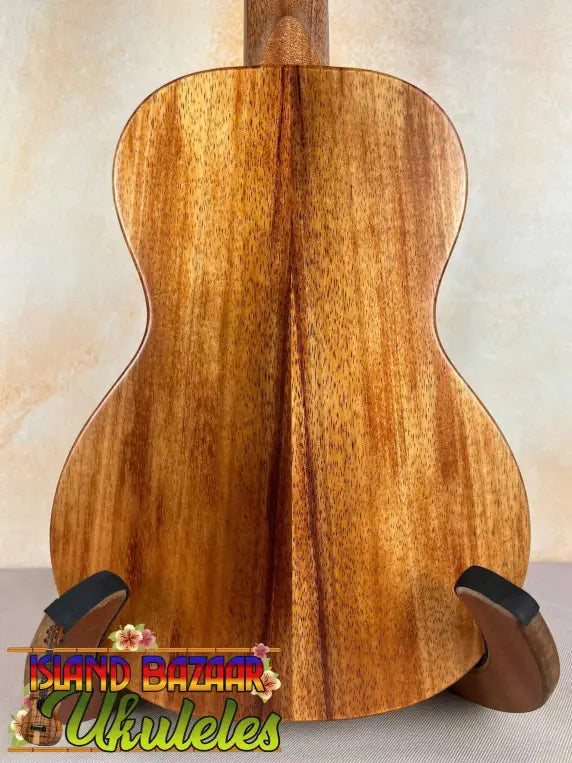 Acoustic guitar with koa wood back panel on stand, showcasing KoAloha Royal Pikake Concert