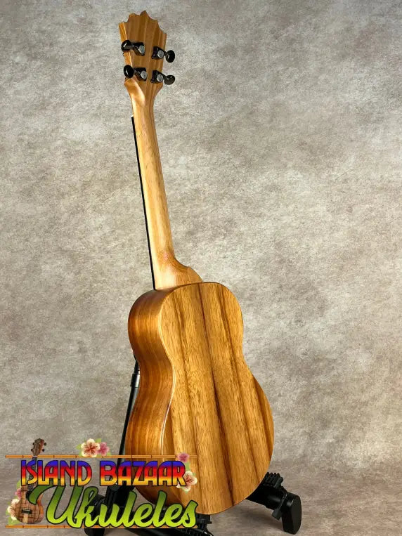 Light brown Koaloha Royal Pikake tenor ukulele with black tuning pegs on a stand