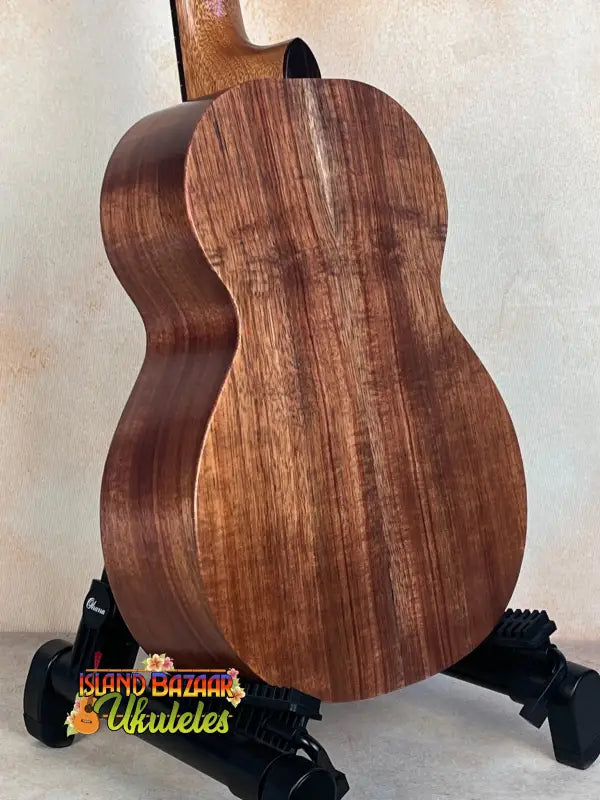 Wooden acoustic guitar on a black stand with Kamaka HF-3I Slothead Tenor Ukulele