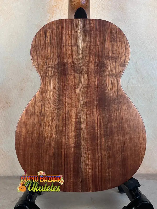 Acoustic guitar with wooden back on black stand, showcases Kamaka HF-3I Slothead Tenor