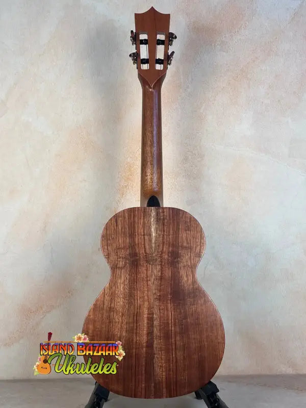 Wooden acoustic guitar with a brown finish on a stand beside Kamaka HF-3I Slothead Tenor