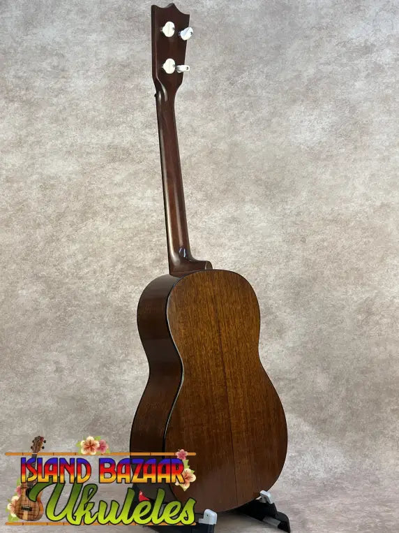 A polished mahogany vintage martin custom baritone ukulele with white tuning pegs standing upright on a black stand