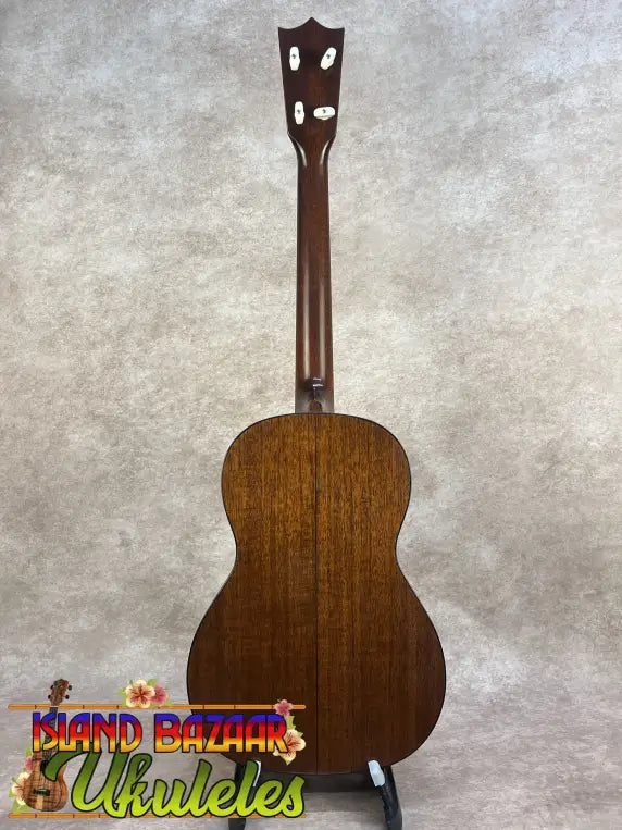 A polished mahogany vintage martin custom baritone ukulele with glossy finish and white tuning pegs on a stand