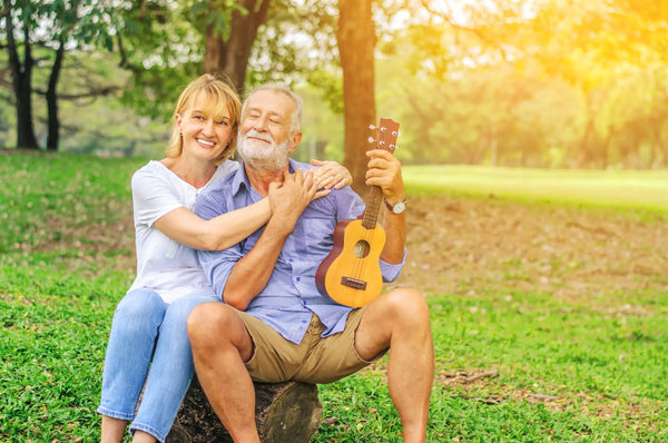 senior couple smiling while holding a ukulele in a sunny park – ukuleles for seniors and joyful strumming