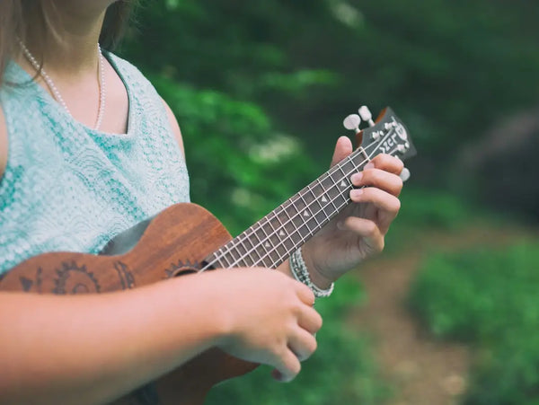 young girl strumming a soprano ukulele outdoors wearing a turquoise dress – beginner ukulele chords for kids