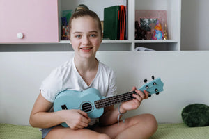 Teen girl playing pastel blue ukulele at home – colorful beginner ukuleles at Island Bazaar Ukes online store