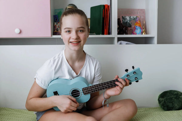 Teen girl playing pastel blue ukulele at home – colorful beginner ukuleles at Island Bazaar Ukes online store