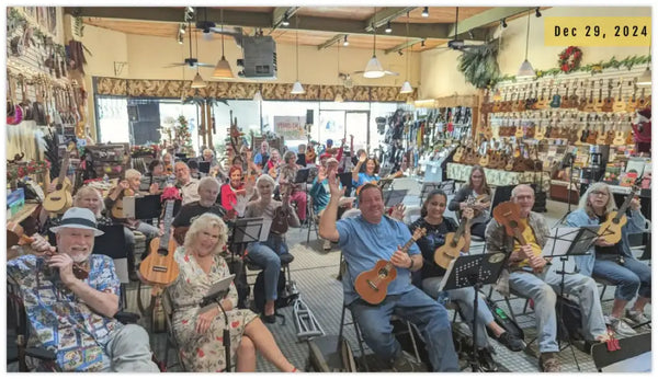 A group of people seated in a music store, each holding and playing ukuleles.