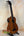 Brown acoustic-electric bass ukulele on a stand, showcasing Kala EM-FS Exotic Macawood Tenor