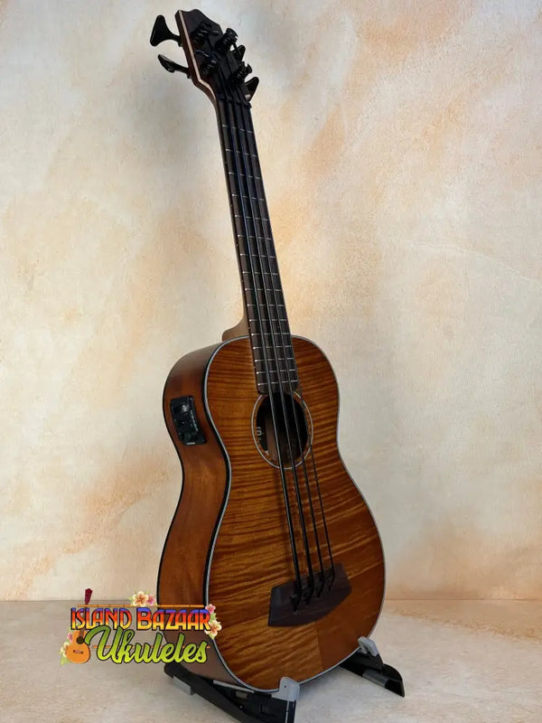 Brown acoustic-electric bass ukulele on a stand, showcasing Kala EM-FS Exotic Macawood Tenor