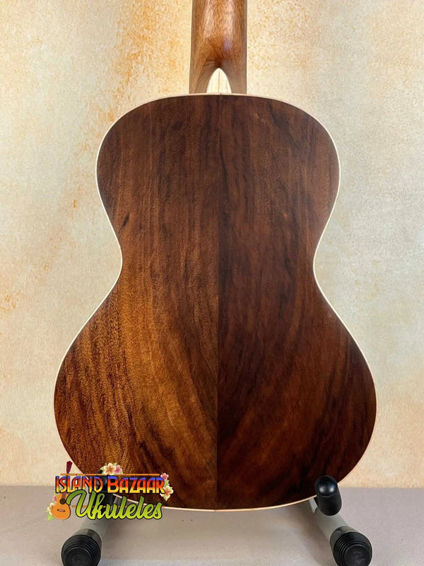 Wooden acoustic guitar on black stand featuring Kala KA-SA-T Acacia Tenor Ukulele design