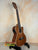 Wooden Kala KA-SMH-TG-CE Tenor Electric Ukulele on a black stand, showcasing solid mahogany