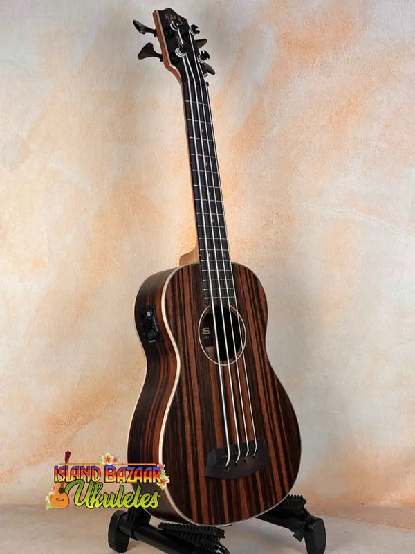 Dark wooden Kala UBASS-EBY-FSRW Striped Ebony Acoustic-Electric Bass Ukulele on black stand