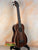 Dark wooden Kala UBASS-EBY-FSRW Striped Ebony Acoustic-Electric Bass Ukulele on black stand