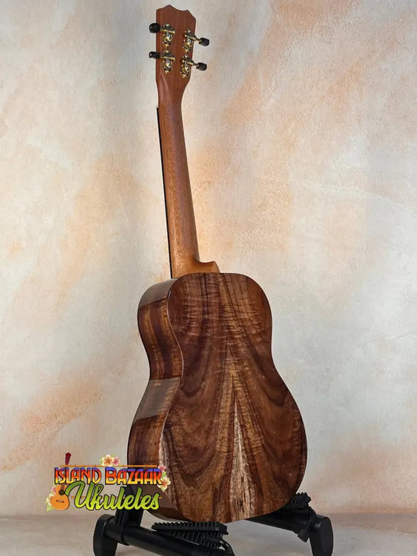 Wooden acoustic guitar on black stand featuring Kanile’a ISL-T Hawaiian Islands Tenor Ukulele