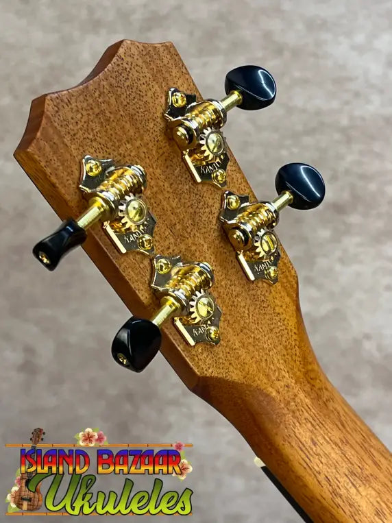 Wooden kanileʻa honus tenor ukulele headstock with gold tuning machines and black pegs on koa concert model