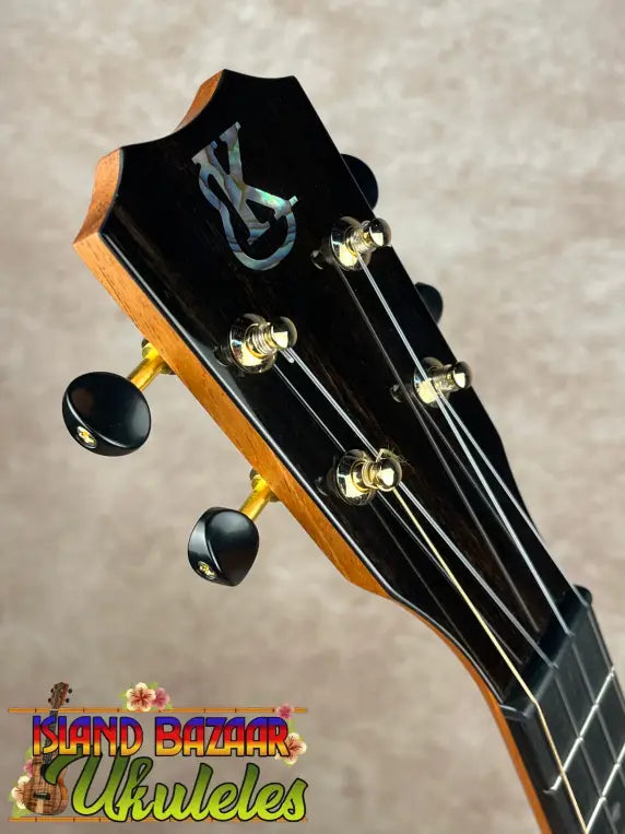 Headstock of Kanile’a KPA Pro Tenor Koa Ukulele with black tuning pegs and mother-of-pearl KS inlay