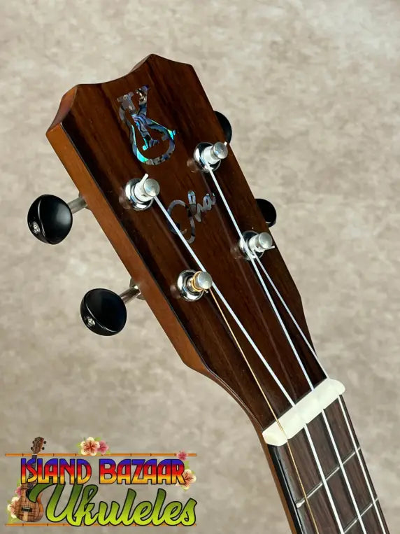 Brown wooden Kanile’a Super Tenor ukulele headstock with black tuning pegs and abalone inlay