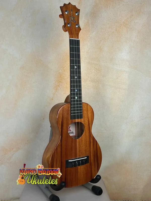 Wooden ukulele with natural finish on stand; KoAloha KCM-00 Concert, Solid Hawaiian Koa