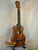 Wooden ukulele with natural finish on stand; KoAloha KCM-00 Concert, Solid Hawaiian Koa