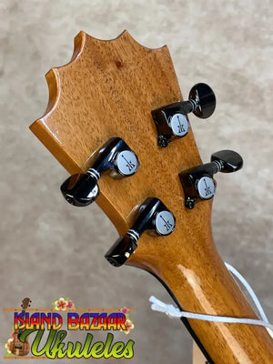 A polished light brown hawaiian koa koaloha ktm-00 tenor ukulele headstock with black tuning pegs and authentic hawaiian sound