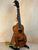 Wooden ukulele with dark grain patterns and black pegs, featuring KoAloha Royal Pikake KCM-00RP