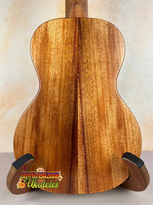 Acoustic guitar with koa wood back panel on stand, showcasing KoAloha Royal Pikake Concert