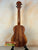 Wooden Koaloha Royal Pikake Tenor Ukulele with natural grain on a black display stand