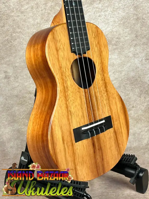 Light-colored wooden Koaloha Royal Pikake Tenor Ukulele with solid Hawaiian koa finish on stand