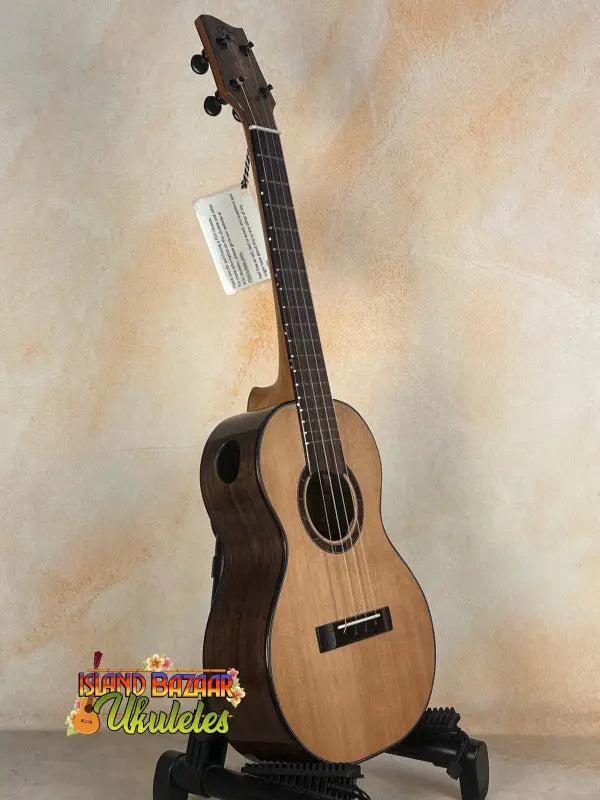 Natural wood Nebula Tenor Ukulele with dark fretboard on a stand, showcasing Claro Walnut craftsmanship