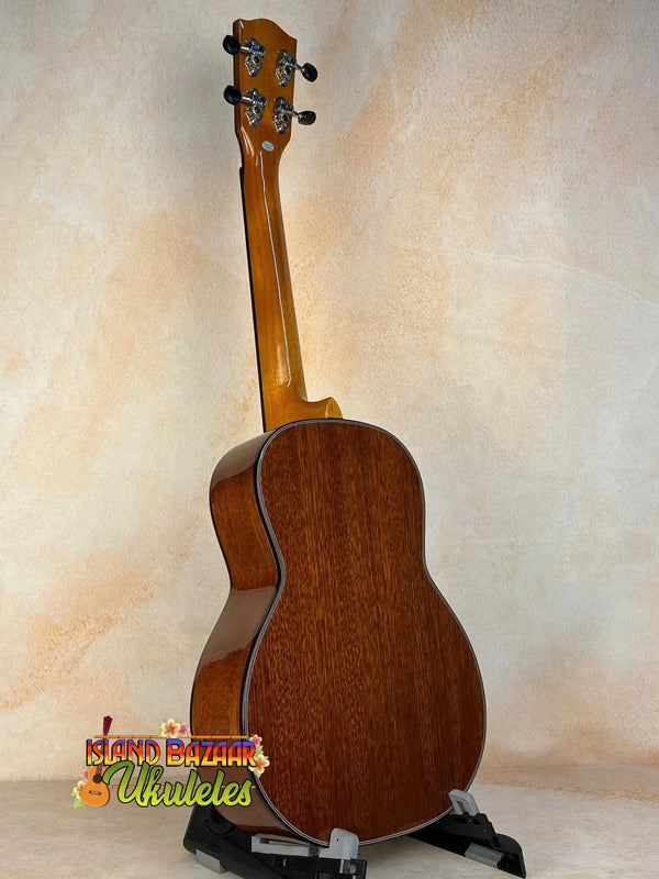 Wooden acoustic guitar on a black stand showcasing Ohana TK-35G Solid Mahogany Tenor Ukulele