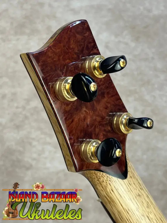 PCH Wickered Oregon Myrtle ukulele headstock with dark reddish-brown wood and gold tuning pegs