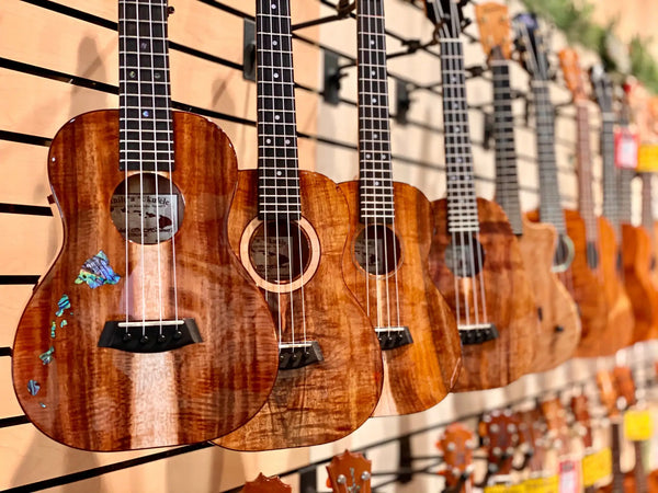 A row of polished, warm-toned wooden ukuleles with dark fretboards and decorative inlays.