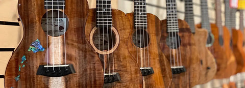 Row of tenor Romero Creations ukuleles showcasing stunning koa wood grain patterns.