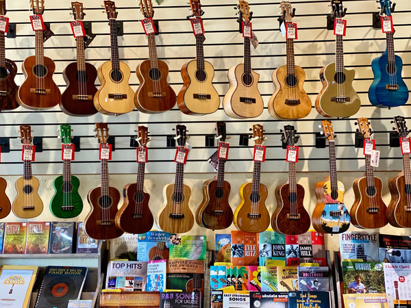 A vibrant blue ukulele with a glossy finish and decorative graphic design hangs on display among other wooden instruments.