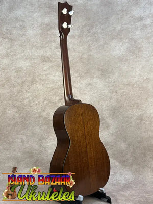 A polished mahogany vintage martin custom baritone ukulele with white tuning pegs standing upright on a black stand